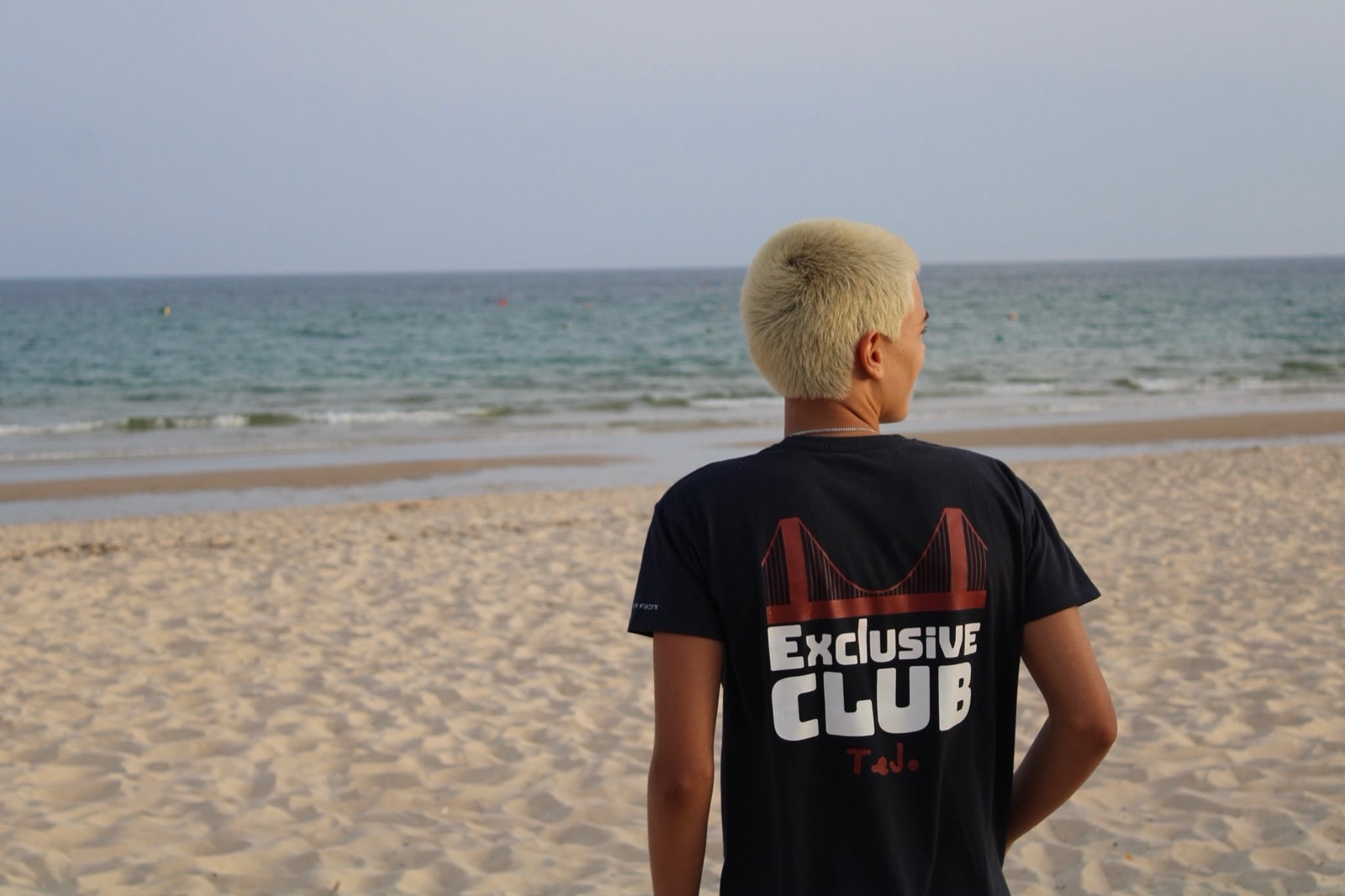 A t-shirt Exclusive Club na praia, vista de costas, com o gráfico da ponte 25 de Abril.